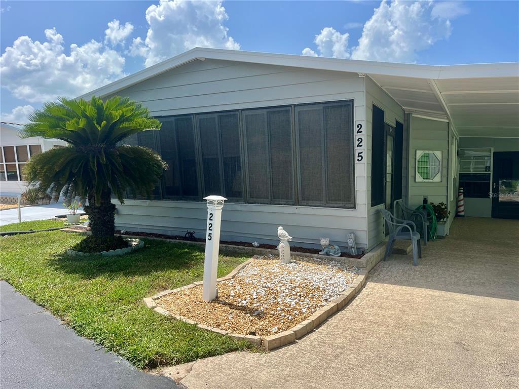 A light green manufactured home features a screened-in porch, a carport, and a palm tree — 225 STARBOARD DRIVE, FLAGLER BEACH, FL