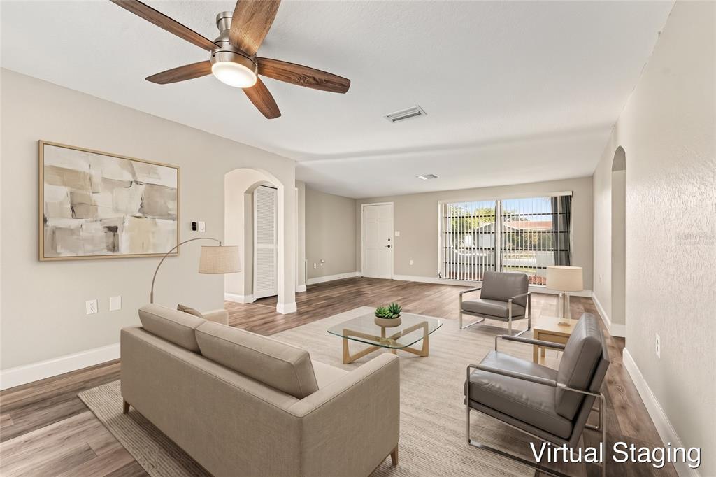 An empty living room features wood-look flooring, a ceiling fan, and sliding glass patio doors — 3207 SALISBURY DRIVE, HOLIDAY, FL