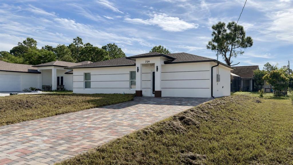 A single-story house with white horizontal-lined siding and a paved driveway under a blue sky — 729 ANACONDA AVENUE S, LEHIGH ACRES, FL