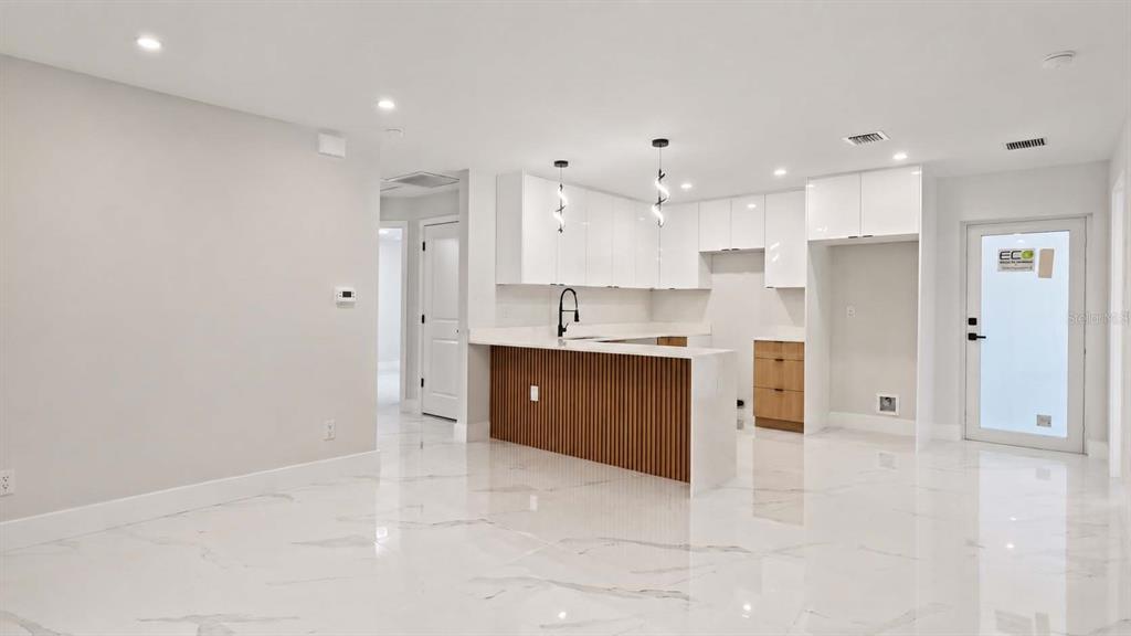 A modern kitchen features white cabinets, a wood-slatted island, and white marble-look tile flooring — 729 ANACONDA AVENUE S, LEHIGH ACRES, FL