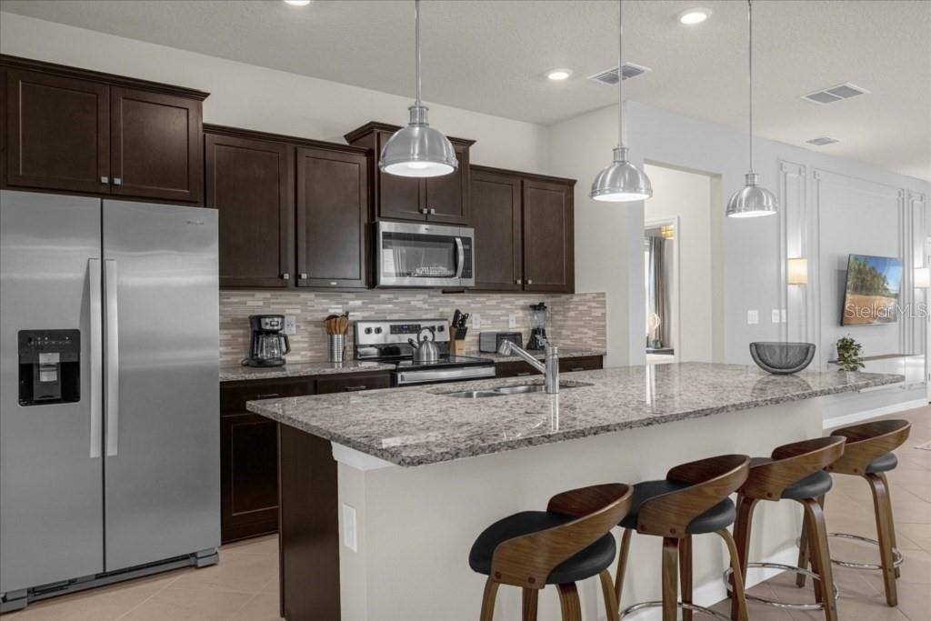 A kitchen with dark wood cabinets, granite countertops, a large island, and stainless steel appliances — 1261 EMERALD ROW STREET, CLERMONT, FL