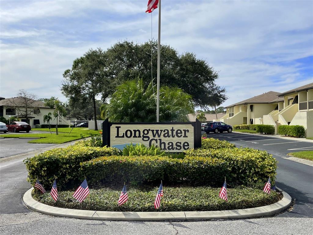 A sign for Longwater Chase stands in a landscaped island with small American flags — 4648 LONGWATER CHASE UNIT 99, SARASOTA, FL