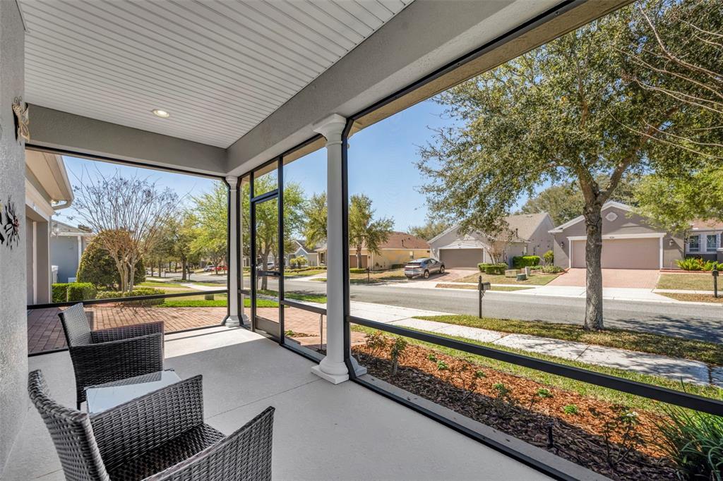 A screened-in front porch features wicker chairs overlooking a suburban street and neighborhood homes — 334 SILVER MAPLE ROAD, GROVELAND, FL