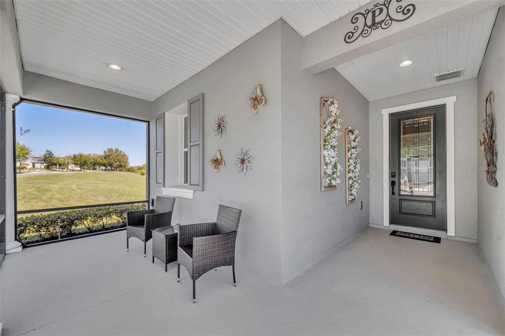 A covered front porch features gray walls, two wicker chairs, and a dark front door — 334 SILVER MAPLE ROAD, GROVELAND, FL