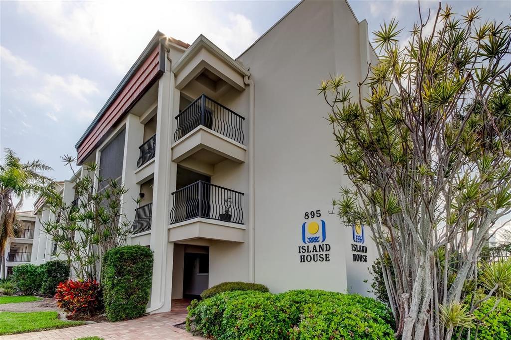 A three-story apartment building exterior with balconies and a sign reading Island House — 895 S GULFVIEW BOULEVARD UNIT 202, CLEARWATER, FL