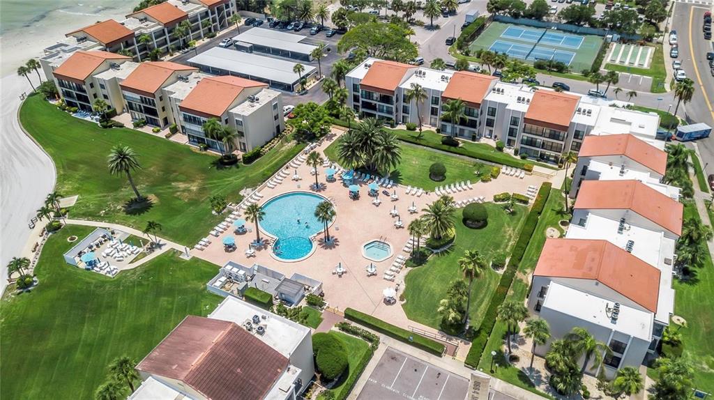 An aerial view of a multi-building apartment complex featuring a central swimming pool and tennis courts — 895 S GULFVIEW BOULEVARD UNIT 202, CLEARWATER, FL