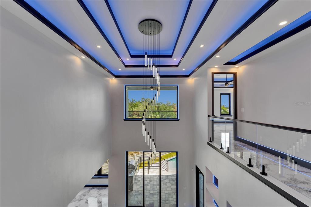A two-story foyer features a spiral chandelier, blue tray ceiling lighting, and a glass balcony — 6520 SIMONE SHORES CIRCLE, APOLLO BEACH, FL