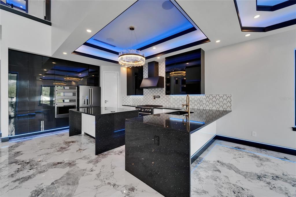 A modern kitchen features black glossy cabinetry, two islands with black countertops, and blue ceiling lighting — 6520 SIMONE SHORES CIRCLE, APOLLO BEACH, FL