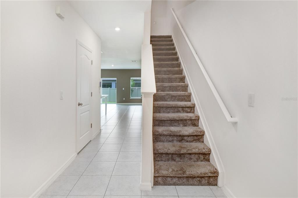 An interior view shows a tiled entryway leading to a carpeted staircase and living area — 32103 POND APPLE BEND, SAN ANTONIO, FL