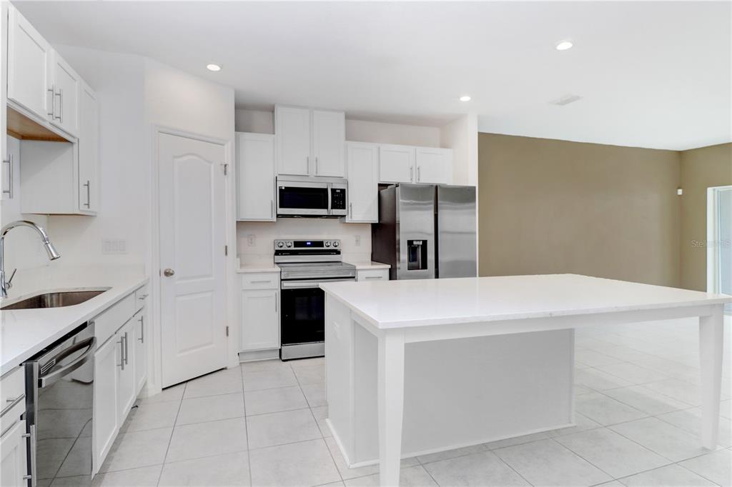 A modern kitchen features white cabinetry, stainless steel appliances, and a large white island — 32103 POND APPLE BEND, SAN ANTONIO, FL