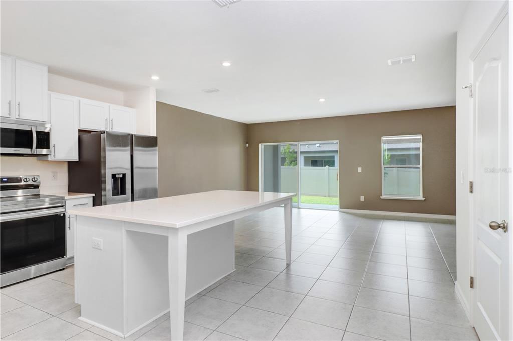 A kitchen with white cabinets and a central island opens into a tiled living area — 32103 POND APPLE BEND, SAN ANTONIO, FL