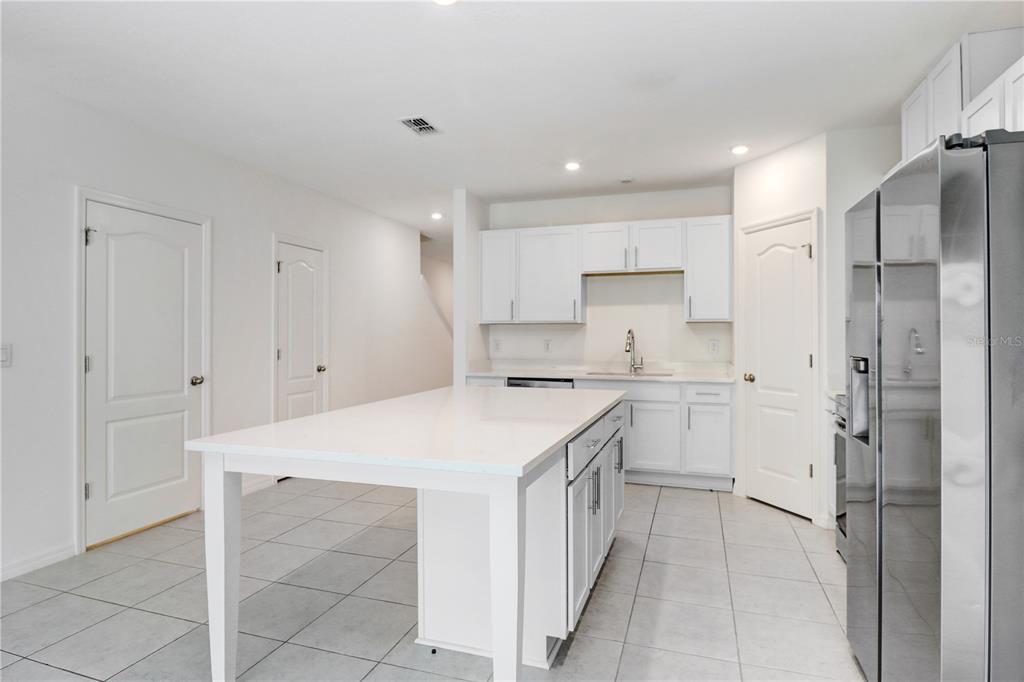 A white kitchen features a central island, stainless steel refrigerator, and light-colored tile flooring — 32103 POND APPLE BEND, SAN ANTONIO, FL