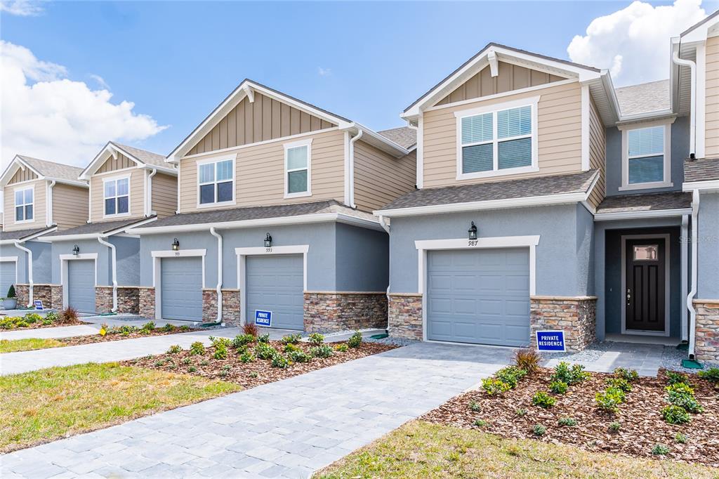 A row of multi-story townhomes with gray garages, stone veneer bases, and tan siding — 987 SPRING PALMS LOOP, ORLANDO, FL