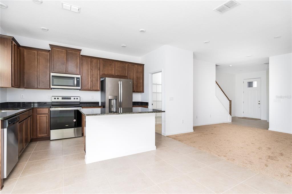 A kitchen with dark wood cabinets, stainless steel appliances, and an island overlooks a carpeted area — 987 SPRING PALMS LOOP, ORLANDO, FL