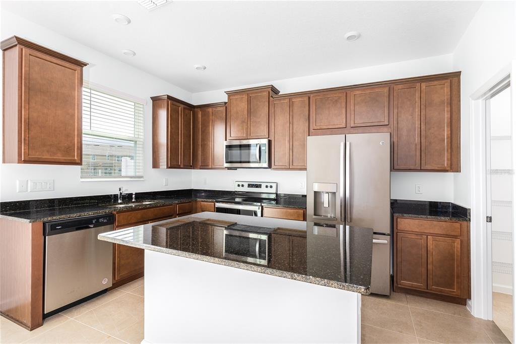 A kitchen features dark wood cabinets, black granite countertops, stainless steel appliances, and a central island — 987 SPRING PALMS LOOP, ORLANDO, FL