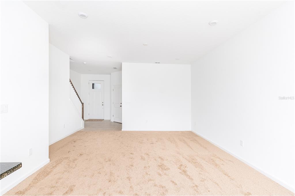 An empty living room features beige carpeting, white walls, recessed lighting, and a staircase — 987 SPRING PALMS LOOP, ORLANDO, FL