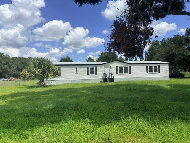 A single-story manufactured home with white siding sits on a grassy lot under a blue sky — 5118 BENNETT DRIVE, LAKELAND, FL
