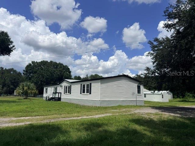 A white manufactured home sits on a grassy lot under a cloudy blue sky — 5118 BENNETT DRIVE, LAKELAND, FL
