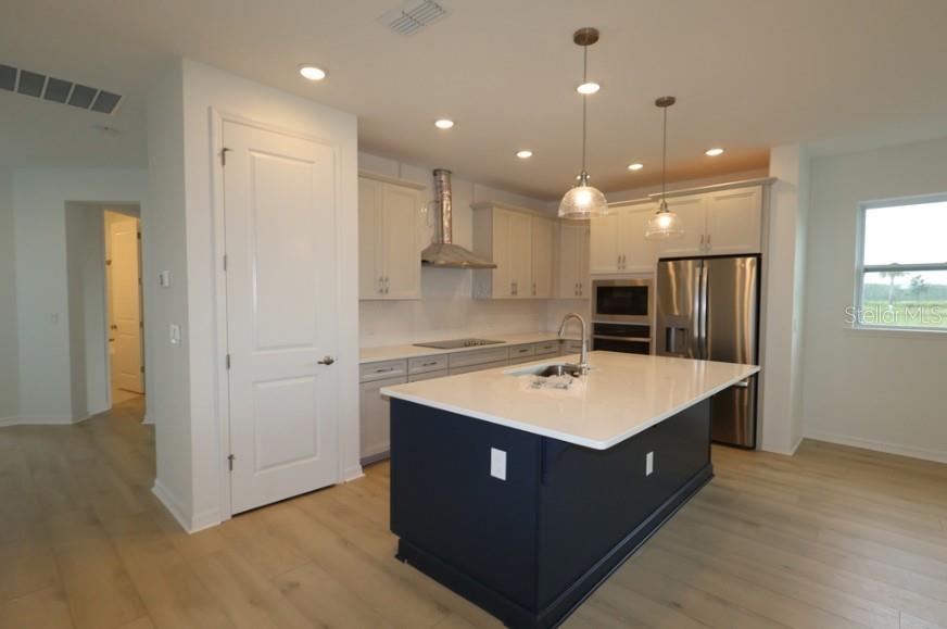 A kitchen features a dark blue island, white cabinets, stainless steel appliances, and light wood flooring — 3219 VOYAGER AVENUE, ST CLOUD, FL