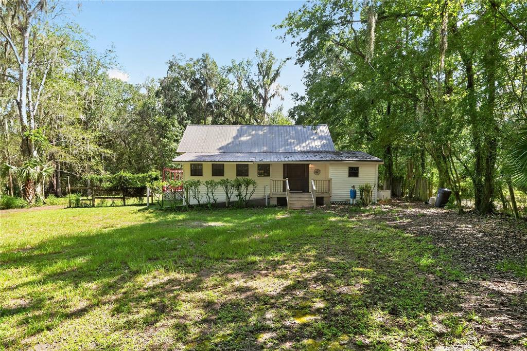 A one-story house with a metal roof sits in a grassy yard surrounded by trees — 9350 NW 230 STREET, MICANOPY, FL
