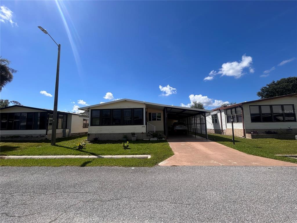 A single-story manufactured home with a carport and a front lawn under a blue sky — 6458 HOLLYBERRY LANE NE, WINTER HAVEN, FL