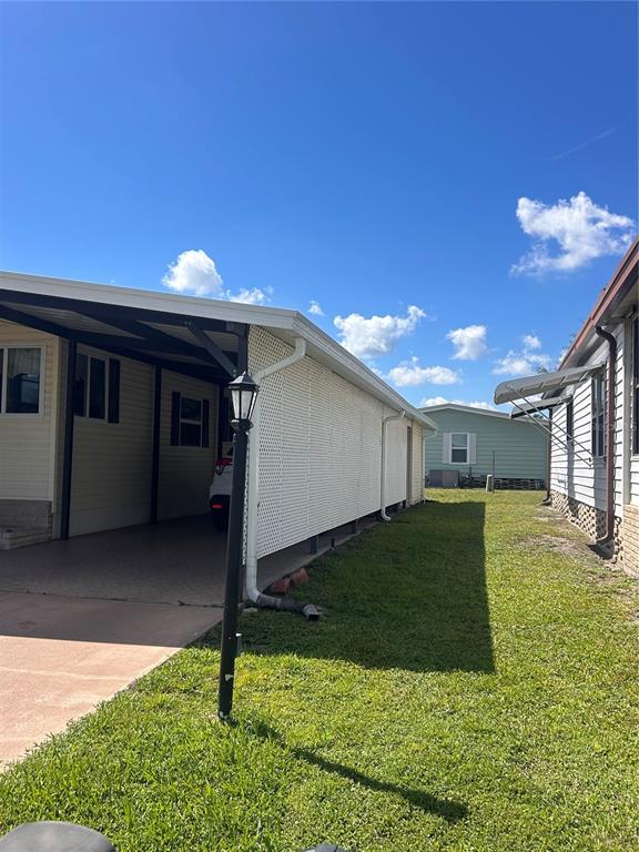 The exterior of a mobile home features a carport, lattice screening, and a grassy yard — 6458 HOLLYBERRY LANE NE, WINTER HAVEN, FL
