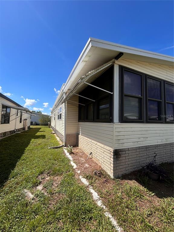 The exterior of a mobile home features light-colored siding, a brick base, and dark-framed windows — 6458 HOLLYBERRY LANE NE, WINTER HAVEN, FL