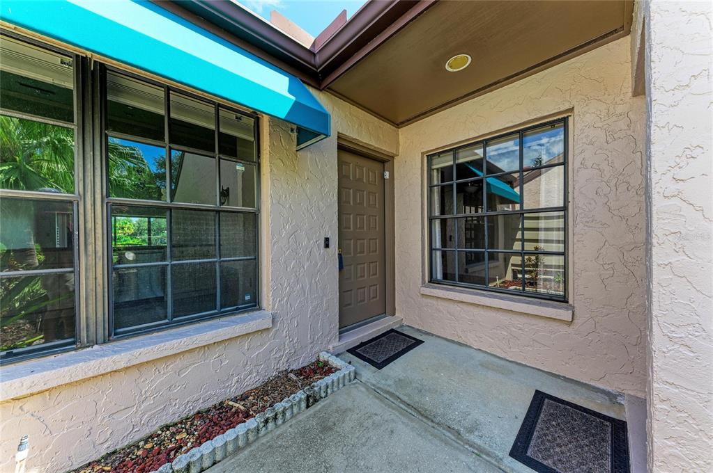 A tan stucco exterior features a brown front door, two grid-pane windows, and concrete flooring — 6085 CLUBSIDE DRIVE, SARASOTA, FL