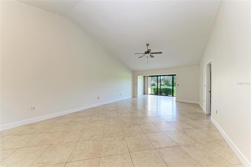 An empty living room with vaulted ceilings, tile flooring, a ceiling fan, and sliding glass doors — 6085 CLUBSIDE DRIVE, SARASOTA, FL