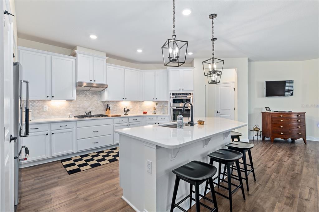A white kitchen features a central island with bar seating, stainless appliances, and wood flooring — 6 SIGNET CIRCLE, FLAGLER BEACH, FL