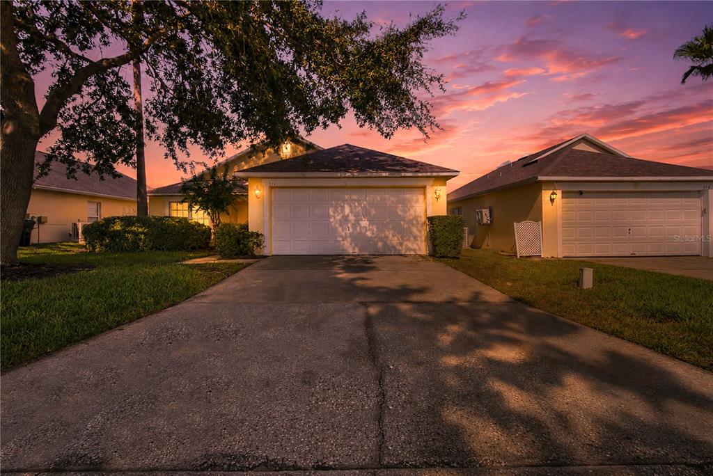 A concrete driveway leads to the two-car garage of a suburban home at sunset — 324 CASTERTON CIRCLE, DAVENPORT, FL