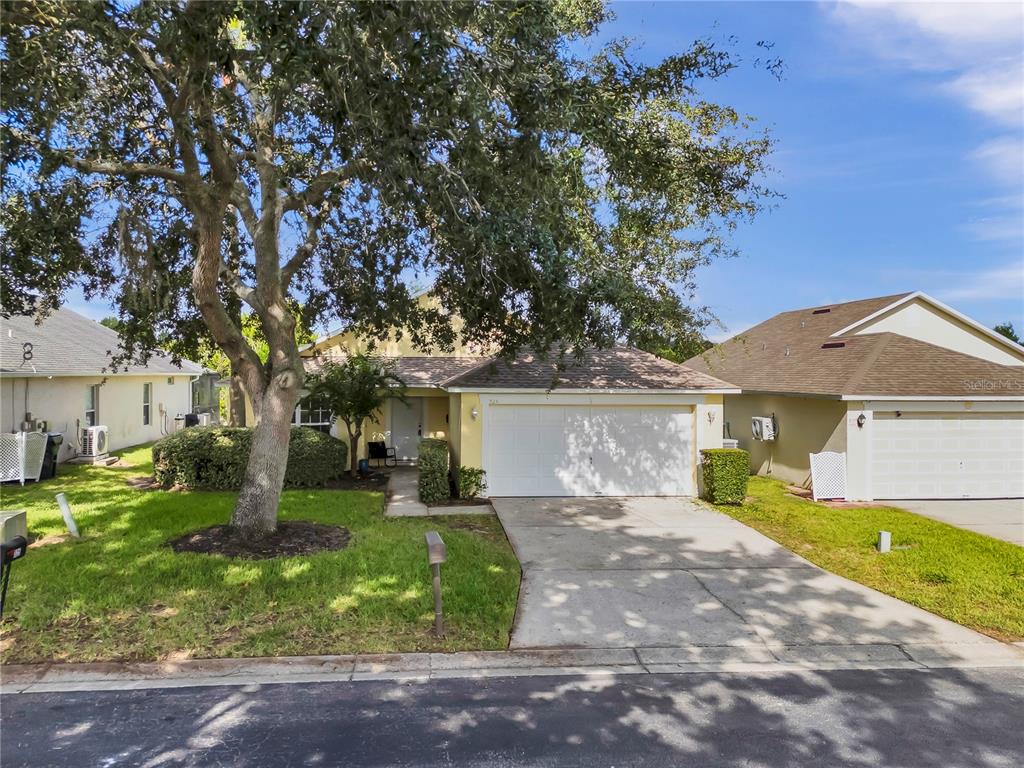 A yellow single-story house with a white garage door and a large tree in front — 324 CASTERTON CIRCLE, DAVENPORT, FL