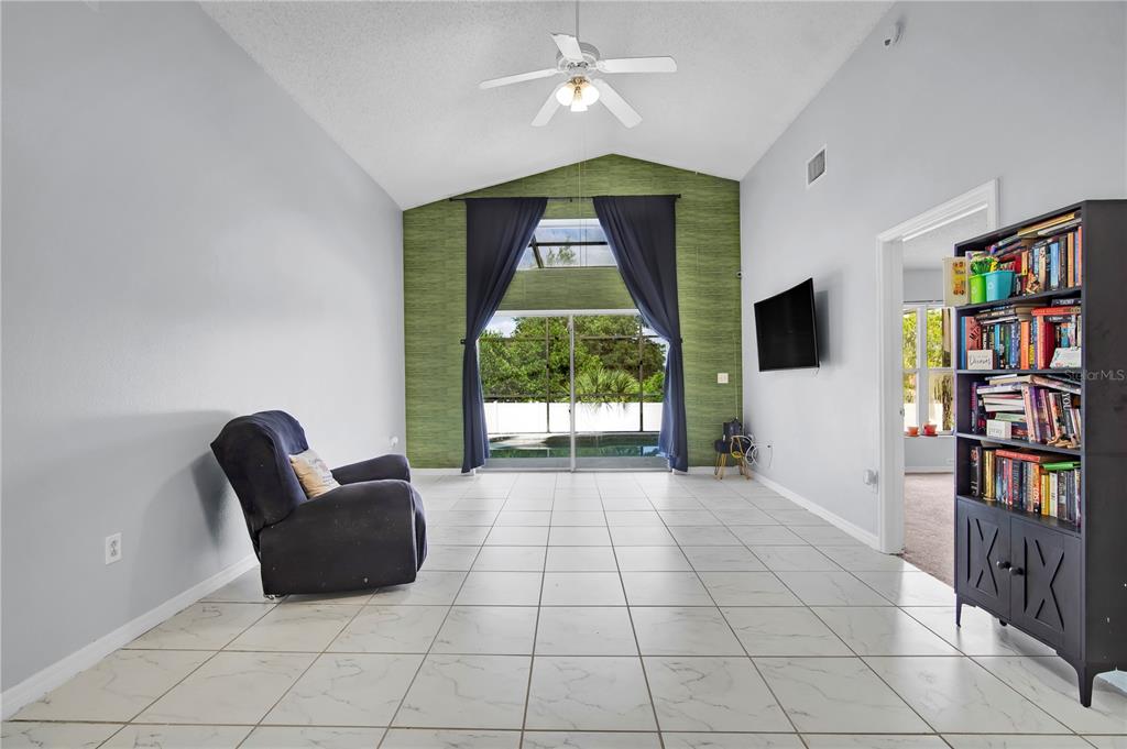A living room with white tile floors, a vaulted ceiling, and a green accent wall — 324 CASTERTON CIRCLE, DAVENPORT, FL