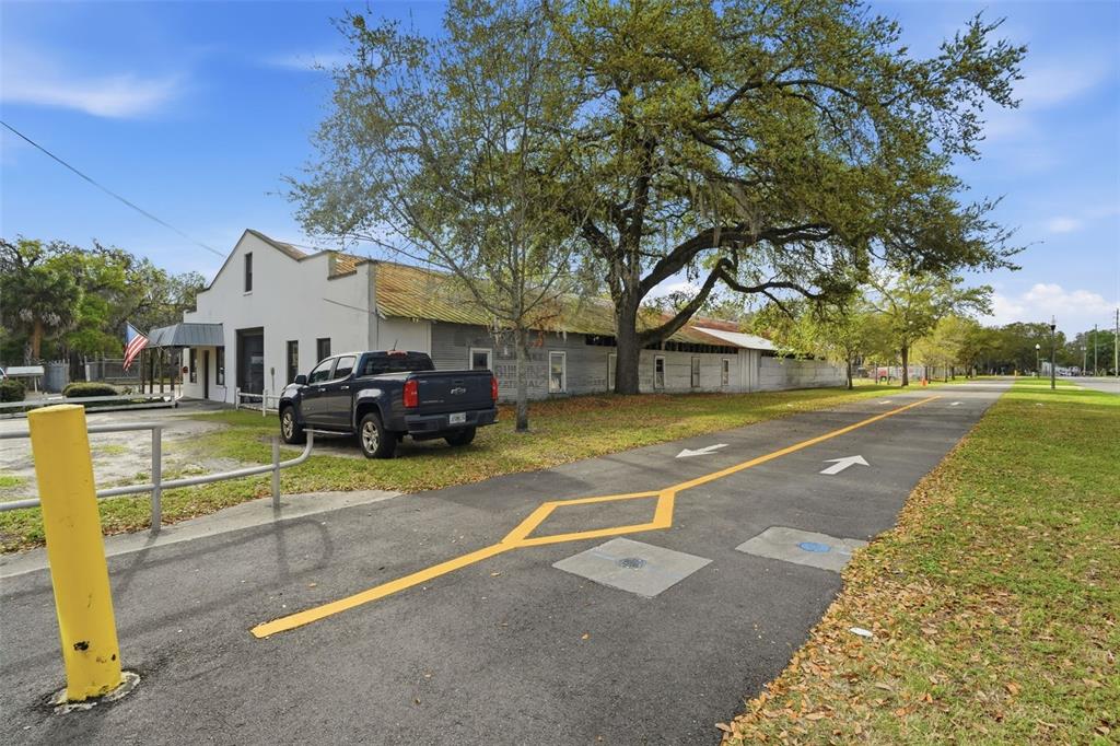 A dark pickup truck is parked next to a long, white industrial building with trees — 210 5TH STREET, APOPKA, FL