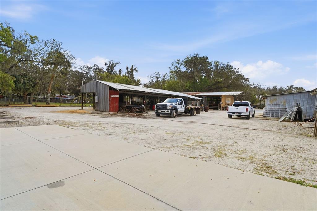 A gravel yard features a large open-sided metal workshop and two parked pickup trucks — 210 5TH STREET, APOPKA, FL