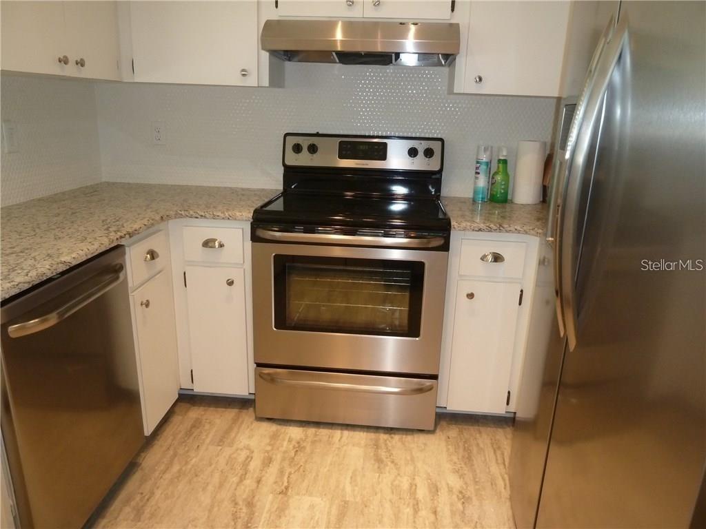 A kitchen features white cabinets, granite countertops, stainless steel appliances, and a tiled backsplash — 212 CARYL WAY UNIT 212, OLDSMAR, FL