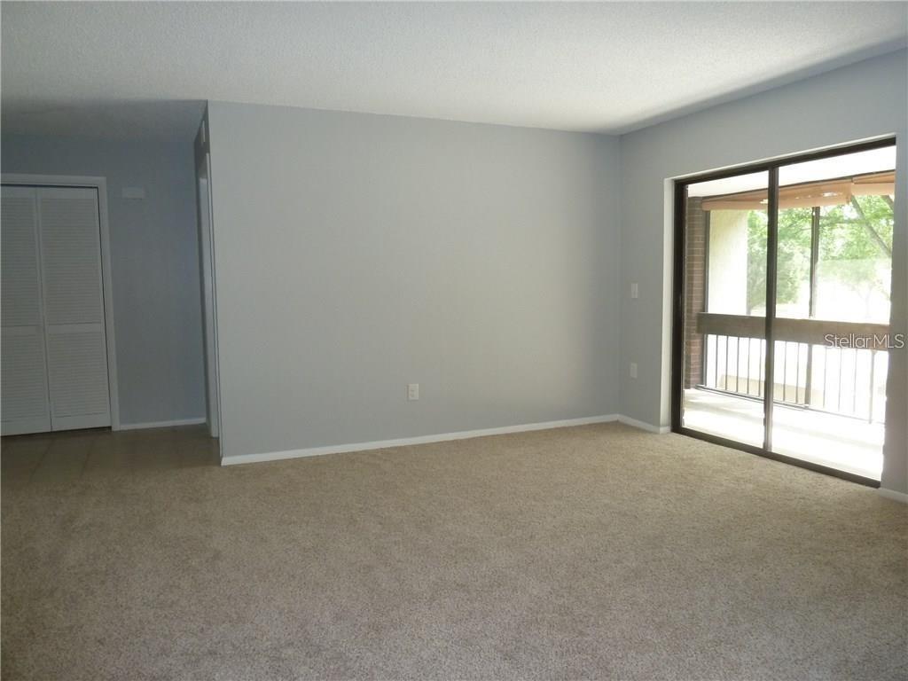 An empty living room features beige carpeting, light gray walls, and a sliding glass door — 212 CARYL WAY UNIT 212, OLDSMAR, FL