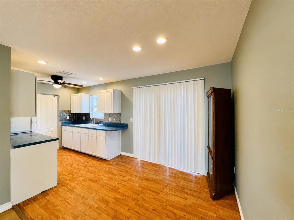 A kitchen with white cabinets, blue countertops, and wood-look flooring opens to a dining area — 12909 LITEWOOD DRIVE, HUDSON, FL