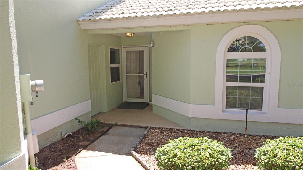 A light green house exterior features a covered entryway, a white arched window, and landscaping — 704 MORAY DRIVE, INVERNESS, FL