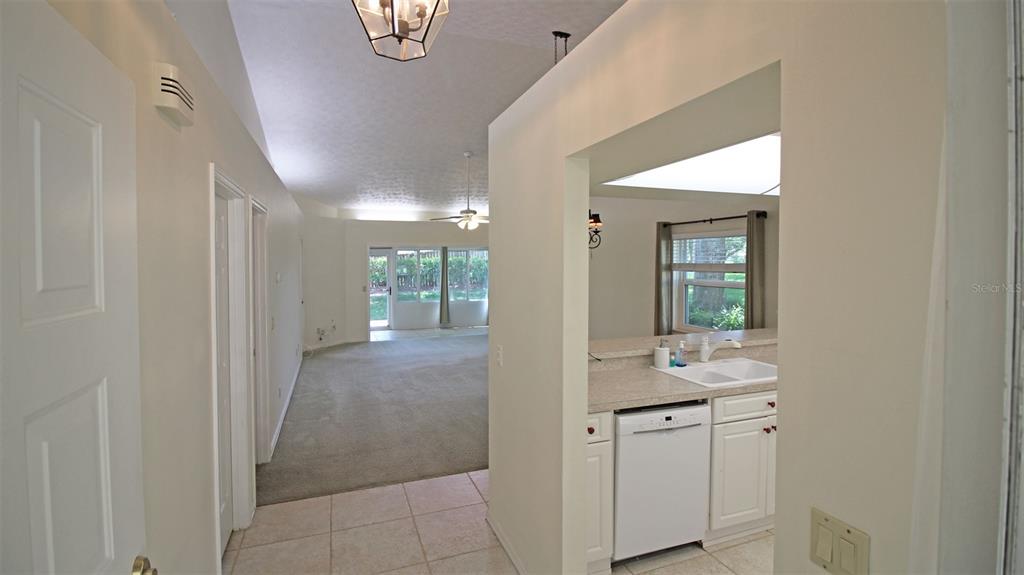 A view from a tiled hallway looking into a carpeted living area and kitchen — 704 MORAY DRIVE, INVERNESS, FL
