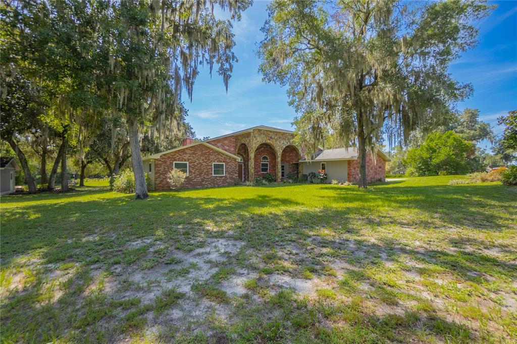 A brick and stone house with arched entryways sits on a large, tree-filled grassy lot — 3711 E TURQUOISE DRIVE, HERNANDO, FL