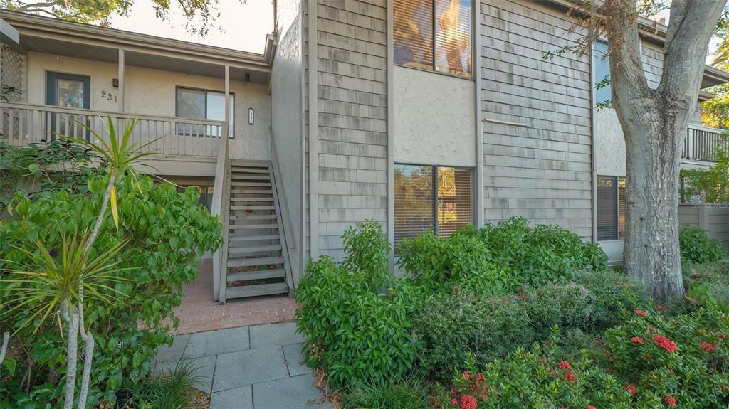 A two-story building exterior features a wooden staircase leading to an upper-level balcony entrance — 1633 BOATHOUSE CIRCLE UNIT HA132, SARASOTA, FL