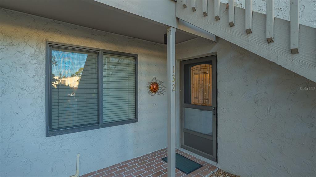 The exterior entrance of a residence features a brick porch, a window, and a screen door — 1633 BOATHOUSE CIRCLE UNIT HA132, SARASOTA, FL