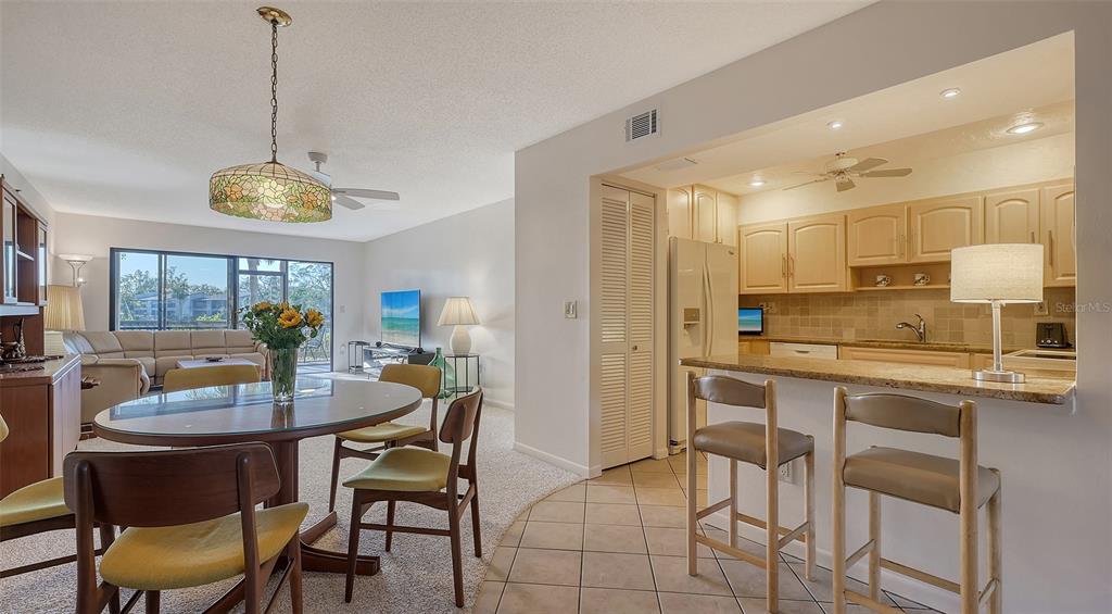 A dining area and kitchen with light wood cabinets, granite countertops, and tile flooring — 1633 BOATHOUSE CIRCLE UNIT HA132, SARASOTA, FL