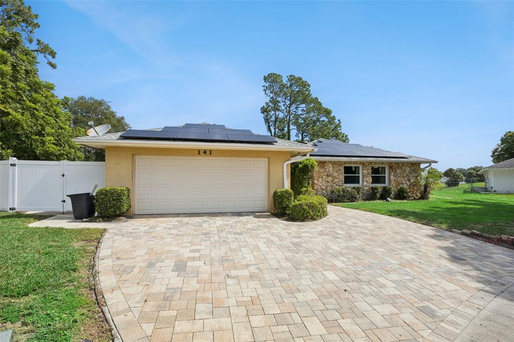 A single-story house with a stone facade, solar panels, and a paved driveway — 141 FAIRWAY TEN DRIVE, CASSELBERRY, FL