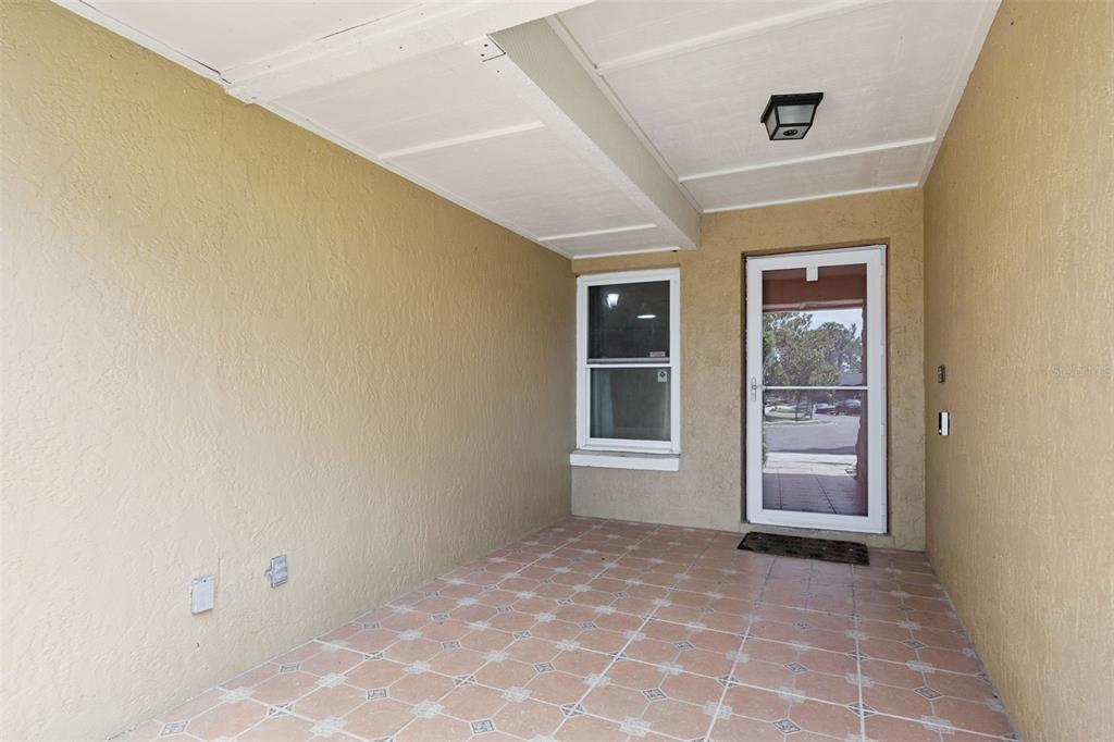A covered outdoor porch features tan stucco walls, a tiled floor, a window, and a door — 141 FAIRWAY TEN DRIVE, CASSELBERRY, FL