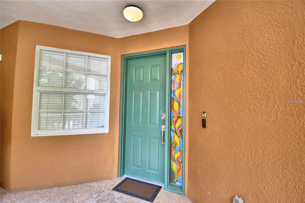 A teal front door with a colorful stained glass sidelight sits beside a white window — 8743 THE ESPLANADE UNIT 8, ORLANDO, FL