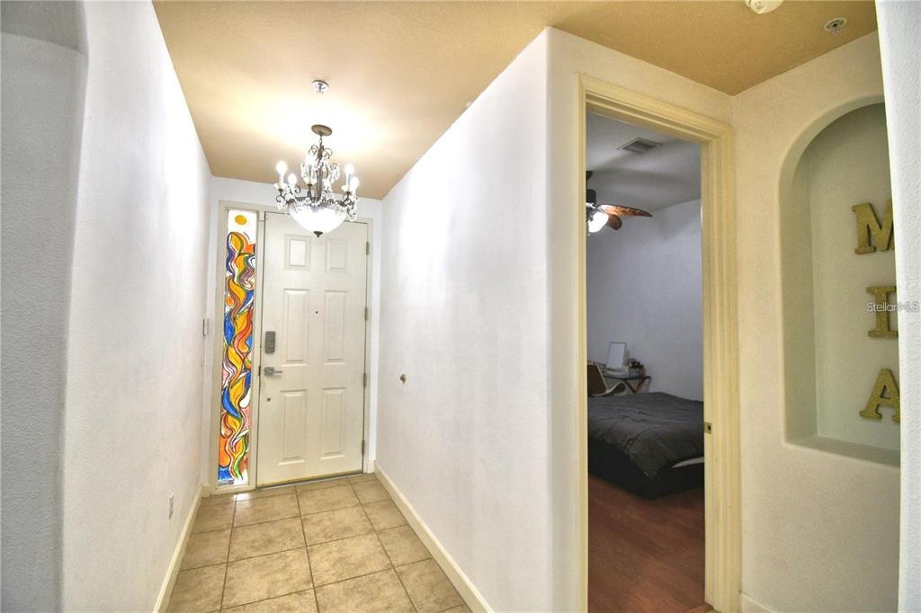 An entryway features a tiled floor, a chandelier, a stained-glass sidelight, and an adjacent bedroom — 8743 THE ESPLANADE UNIT 8, ORLANDO, FL