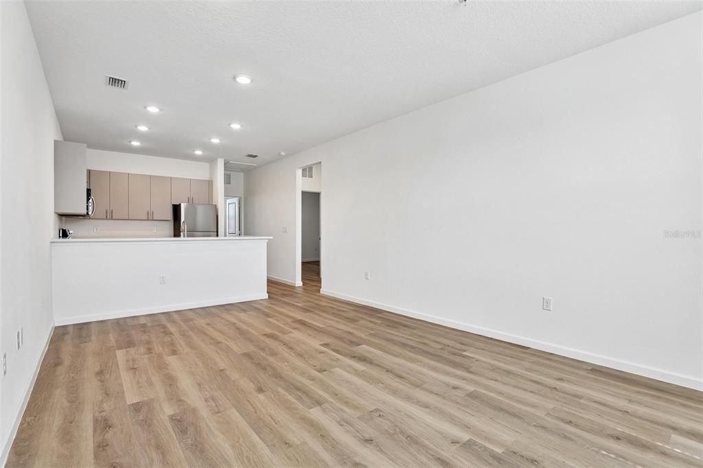 An open-concept living area features light wood-look flooring and a kitchen with neutral cabinets — 3065 SOLDIER CITY WAY UNIT 201, ST CLOUD, FL