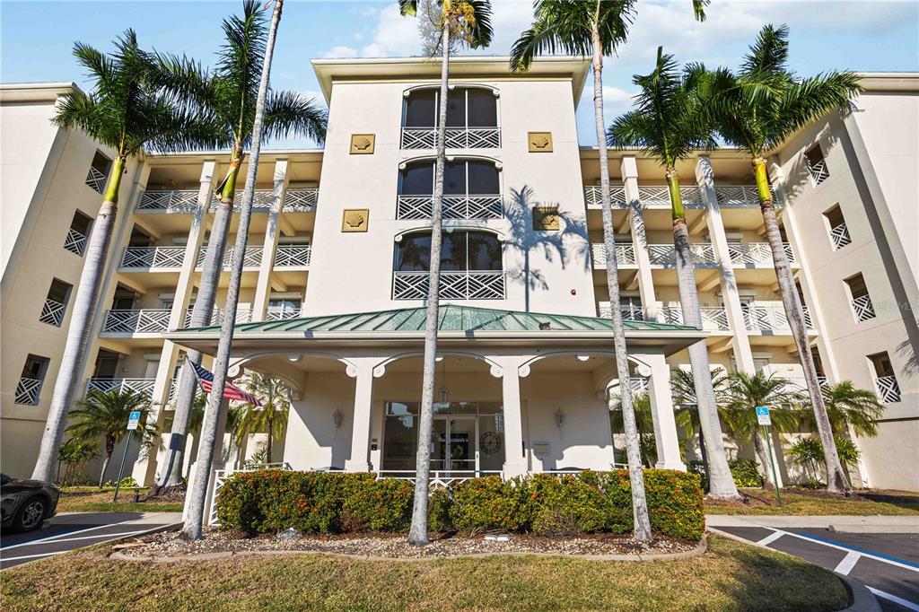 A multi-story beige apartment building with a covered entrance and palm trees in front — 200 HARBOR WALK DRIVE UNIT 322, PUNTA GORDA, FL